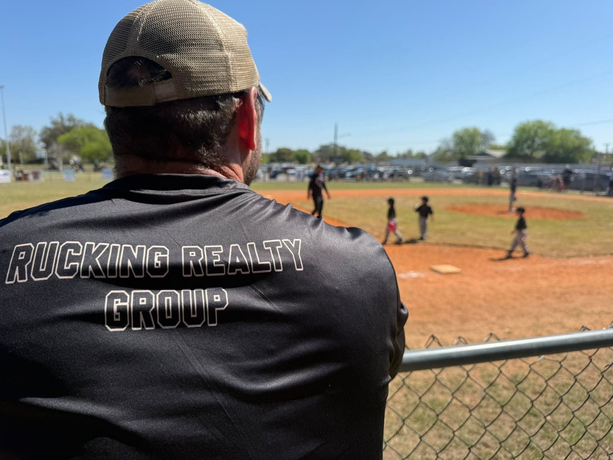 Mike watching a baseball game, wearing a Rucking Realty Group shirt