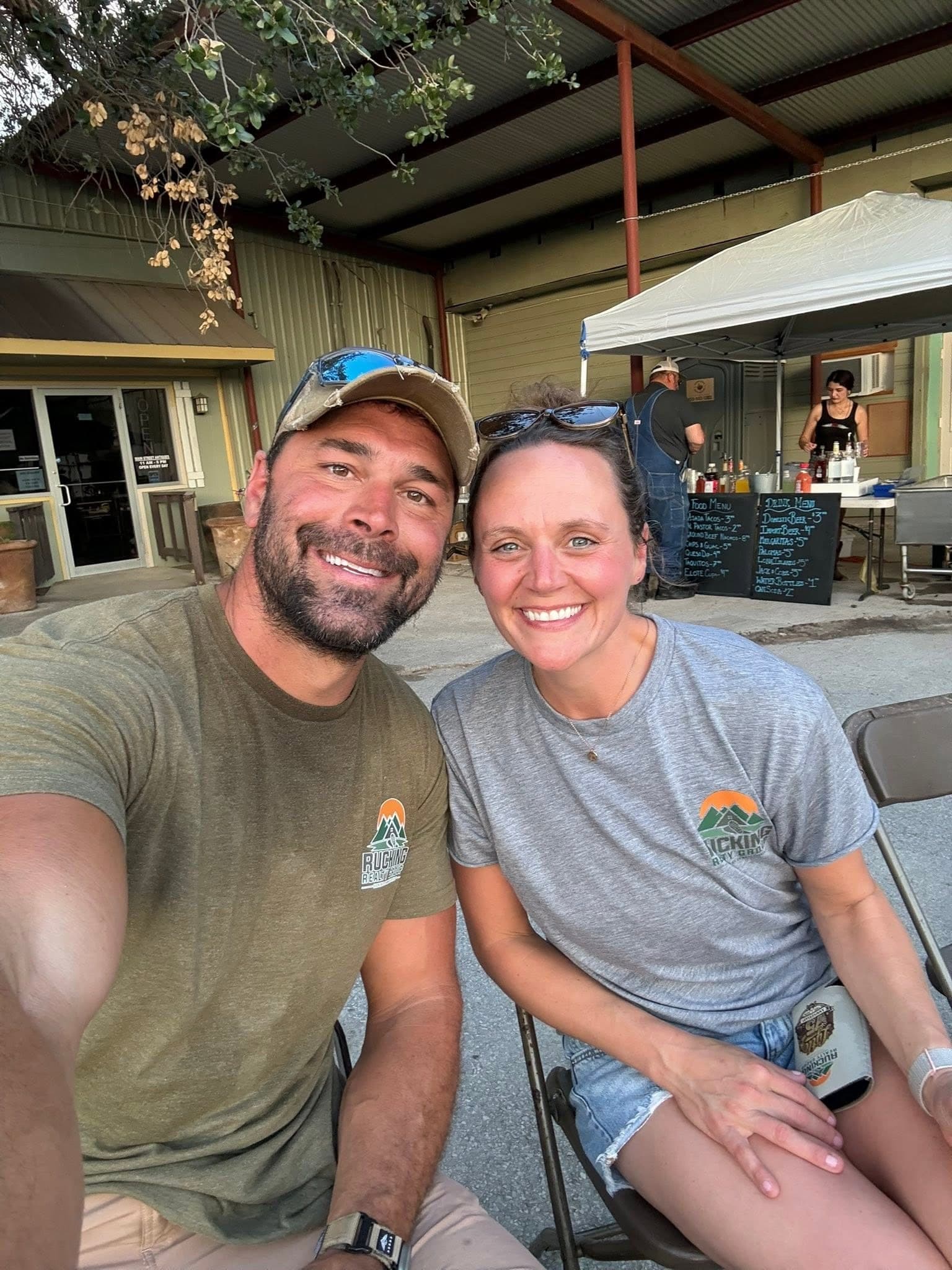 Mike and Natalie Evans in Rucking Realty Group shirts at an outdoor table on a small-town main street